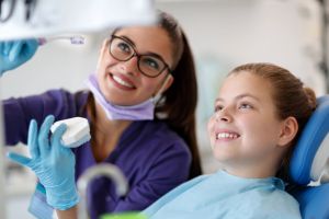 Smiling young girl seated with orthodontist assistant