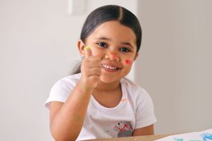 Smiling young girl fingerpainting with thumbs up